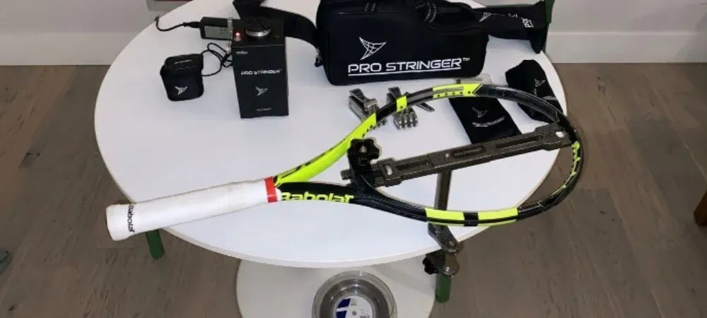 Een tennisracket met een bespanmachine, klemmen, een rol snaar en een reistas op een tafel